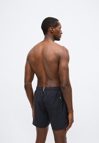 Čierne plavecké šortky s elastickým pásom a jedným zadným vreckom. Materiál pôsobí ľahko a hladko, navrhnutý pre pohodlie.