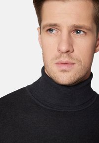 Czarny sweter z golfem o prążkowanej fakturze, z wysokim kołnierzem i dopasowanym krojem, noszony przez modela z krótkimi włosami i zarostem.