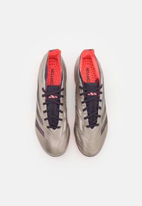 Scarpe da calcio grigie con accenti viola e rosso neon. Design elegante, superficie texturizzata e lacci neri. Loghi in evidenza e dettagli di ventilazione.