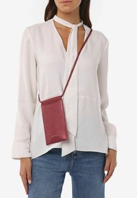 Rode glittercrossbody pouch met een lange schouderband, gecombineerd met een witte blouse en blauwe denim jeans, met een eenvoudig ontwerp en strakke lijnen.