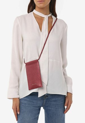 Rød glitrende crossbody pouch taske med en lang rem, parret med en hvid bluse og blå denim jeans, der har et enkelt design og rene linjer.