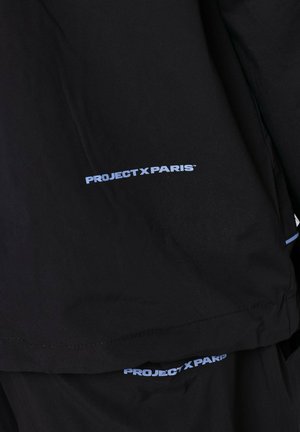 Giubbotto nero con logo "PROJECT X PARIS" in azzurro sul lato sinistro. Texture liscia, vestibilità moderna, design minimalista.