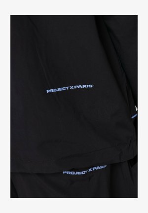 Schwarze Jacke mit dem "PROJECT X PARIS" Logo in hellblau auf der linken Seite. Glatte Textur, moderner Schnitt, minimalistisches Design.