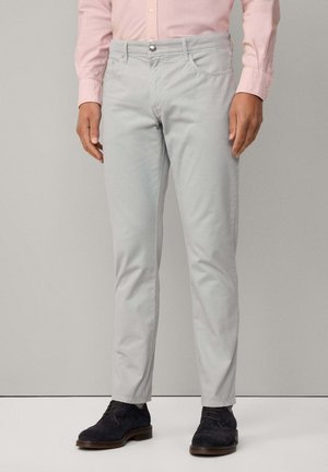 Lys grå chinos i slim fit, med knaplukning, bæltestropper, frontlommer og en glat tekstur. Mørke sko fuldender looket.