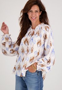 Witte blouse met blauw en bruin abstract patroon, elastische manchetten en een geplooide halslijn. Gekocht in combinatie met blauwe spijkerbroek.