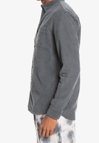 Szara koszula zapinana na guziki, wykonana z miękkiej bawełny, z kieszenią na piersi, standardowym kołnierzykiem i długimi rękawami z guzikami przy mankietach.