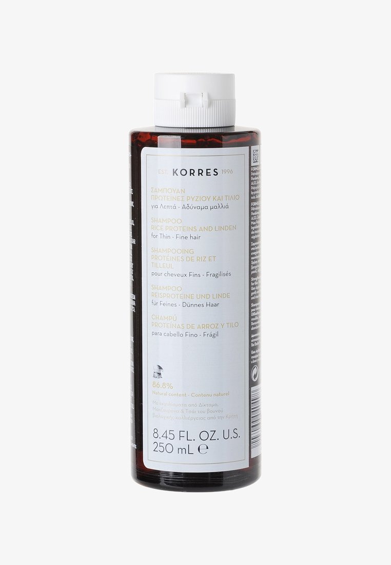 Transparente zylindrische Flasche mit Shampoo, bernsteinfarbig, mit weißem Deckel, mehrsprachigem Etikett und Text, der Reisproteine und Linden hervorhebt.