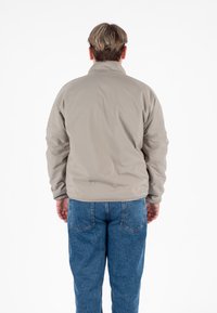 Jasny beżowy pikowany płaszcz z wysokim kołnierzem i długimi rękawami, charakteryzujący się gładką teksturą i dopasowaną talią, noszony na niebieskich dżinsach.