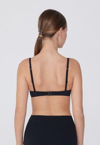 Černá krajková podprsenka s nastavitelnými ramínky, hladkým materiálem a zapínáním na háček a oko na zadní straně. Minimalistický design, bez ozdob.