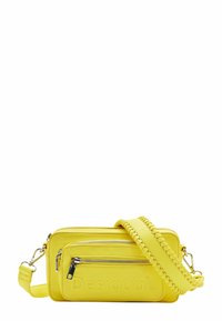 Żółta syntetyczna torba na ramię z dwoma zamykanymi na zamek przegrodami, wytłoczonym logo i plecionym paskiem dla dodatkowej tekstury i detali.
