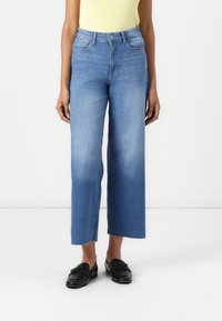 Light blue denim wide-leg jeans with a high waist, five pockets, and frayed hem. Paired with black loafers and a yellow top.