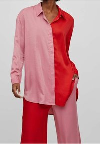 Camicia a maniche lunghe con design color block, con un lato rosa e l'altro lato rosso. Realizzata in tessuto leggero e liscio con colletto con bottoni.