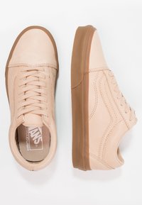 Paire de baskets Vans beige avec semelles en caoutchouc marron, une chaussure vue de dessus et l'autre de côté, sur fond blanc.