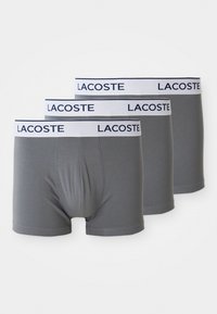 Boxers gris avec une ceinture élastique blanche comportant l'inscription "LACOSTE" en bleu marine. Tissu doux et design ajusté. Lot de trois.