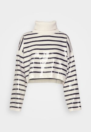 Biała i granatowa w paski krótka bluza z wysokim kołnierzem, zestawiona z luźnymi szarymi spodniami i białymi sneakersami. Trzymana brązowa torba na ramię.