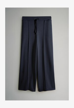 Sügavsinised laia säärega püksid, valmistatud pehmest kangast, millel on nööriga talje ja esipleegid lisadetailiks. Sile ja kerge tekstuur.