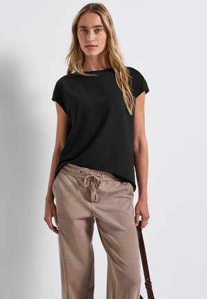 Schwarzes Oberteil mit kurzen Ärmeln und lockerer Passform, kombiniert mit beigen Pants mit Kordelzug, die eine glatte Textur und ein einfaches Design aufweisen.