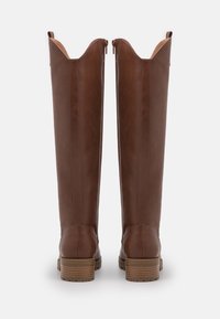 Marron nahkasaappaat, joissa on pyöristetty nenä, sivuvetoketju ja teksturoitu lohkokorko. Korostaa lievää aaltoilevaa yläreunaa.