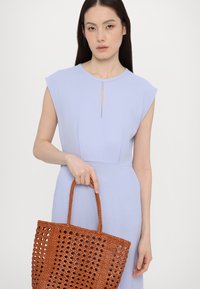 Rochie lavandă deschisă cu decolteu in formă de cheie și mâneci scurte, asortată cu o geantă de umăr din ratan de culoare maro, cu un design texturat și perforat.