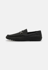 Sorte mokkasinsko-style sko lavet af blødt ruskind, med en dekorativ frontspænde, slip-on design og struktureret gummisål.