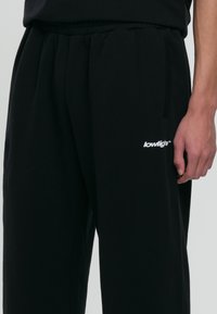 Svarta sweatpants med elastisk midja och sidofickor. Har en vit logga tryckt på vänster lår. Mjuk tygkvalitet.