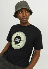 Zwarte katoenen T-shirt met een cirkelvormige afbeelding in lichtgroen met de tekst "JACK & JONES" en "Expedition 9" in het midden.