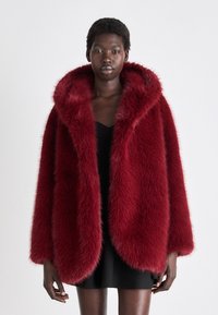 Burgunderfarget faux fur kåpe med stor hette, som har en pusete tekstur og oversize passform, supplert med åpne ermer og en jevn fôr under.