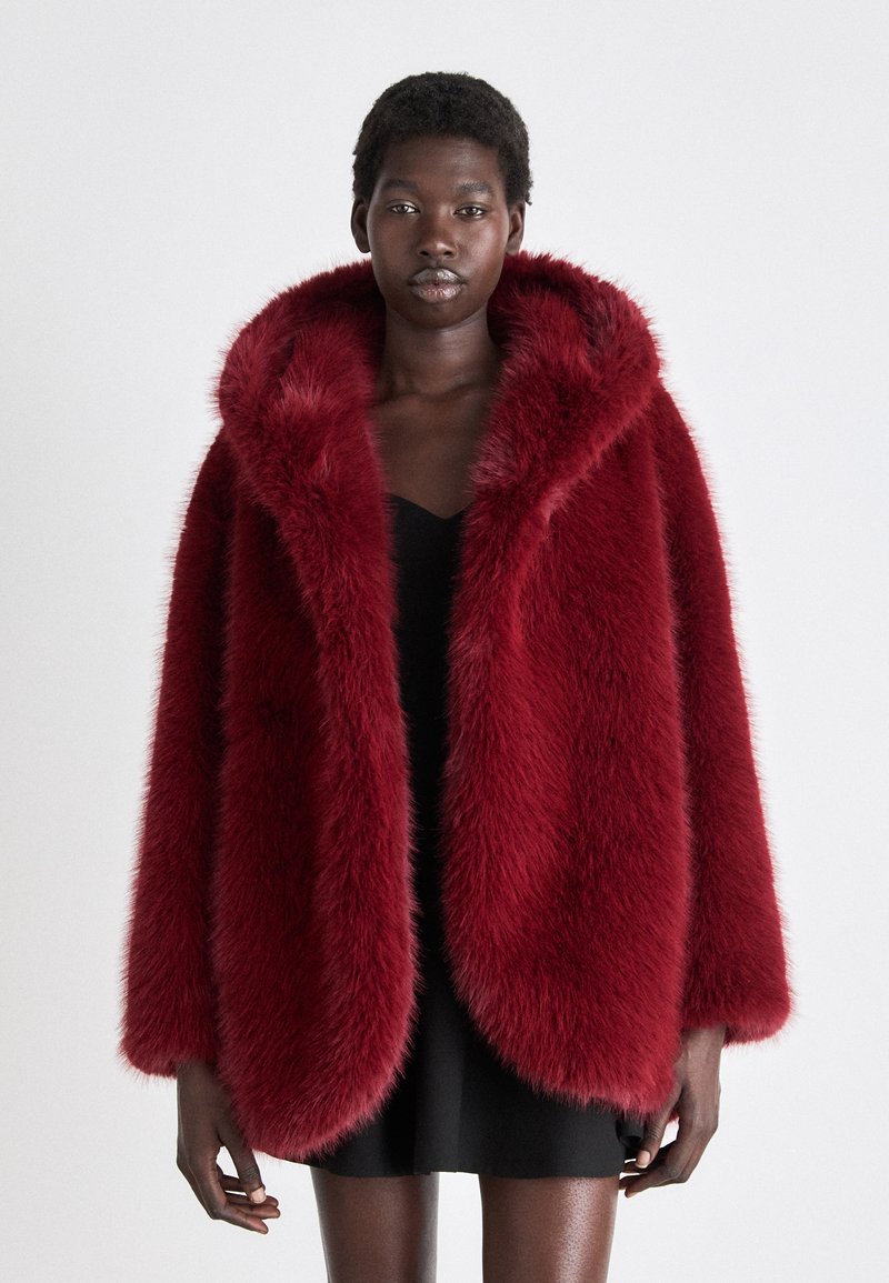 Burgunderfarget faux fur kåpe med stor hette, som har en pusete tekstur og oversize passform, supplert med åpne ermer og en jevn fôr under.