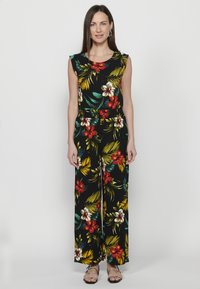 Jumpsuit nero con stampa floreale caratterizzata da fiori rossi e gialli. Design senza maniche, vestibilità rilassata e pantaloni a gamba larga. Tessuto liscia.
