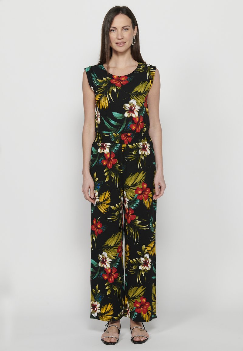 Jumpsuit nero con stampa floreale caratterizzata da fiori rossi e gialli. Design senza maniche, vestibilità rilassata e pantaloni a gamba larga. Tessuto liscia.