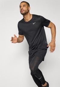 Black Nike athletic shirt with short sleeves, textured fabric, paired with black shorts and compression leggings, featuring a subtle logo.