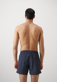 Șorturi de baie bleumarin cu talie elastică și un singur buzunar pe spate, fabricate dintr-un material ușor, texturat.