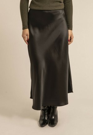 Jupe en satin noir à la texture lisse, avec une fente sur le côté. Associée à des bottes à talons noires, elle présente une taille cintrée et une coupe fluide.