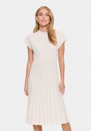 Knit dress featuring a ribbed texture, light beige color, short cap sleeves, and a flared, pleated skirt that falls below the knee.