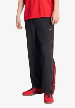 Persona che indossa pantaloni da ginnastica neri Adidas con strisce rosse e scarpe da ginnastica Adidas rosse, abbinati a una maglietta rossa.