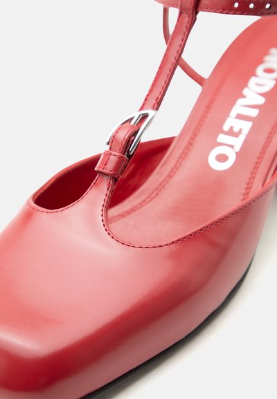 Κόκκινο δερμάτινο παπούτσι σε στυλ Mary Jane με ασημένια αγκράφα και εμφανές όνομα μάρκας "MODALETTO" στο εσωτερικό της σόλας.
