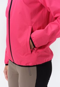 Lätt rosa jacka med dragkedja fram och elastiska ärmbågar; har en dold ficka. Kombinerad med beiga och svarta tajta leggings.