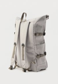 Γκρι υφασμάτινο σακίδιο με ρυθμιζόμενους ιμάντες, πλευρικές τσέπες και σχεδιασμό με ρολό στο πάνω μέρος. Διαθέτει ανθεκτικό εξοπλισμό και λεία υφή.