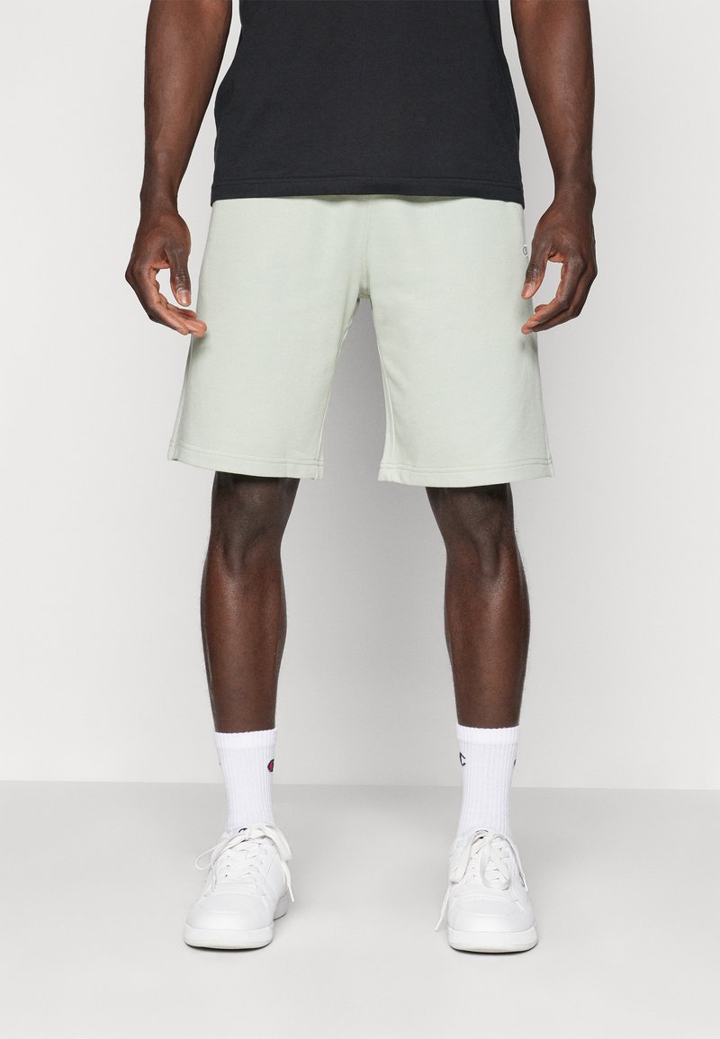 Light green cotton shorts with a relaxed fit, featuring side pockets and visible stitching, paired with white shoes and socks.