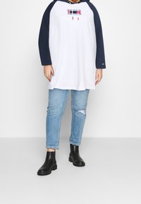 Abito felpa bianco con maniche blu navy, grafica frontale e lacci. Jeans azzurri strappati. Stivali Chelsea neri. Outfit semplice e casual.