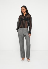 Διαφανές μαύρο πουκάμισο με κουμπιά και μακριά μανίκια, συνδυασμένο με ανοιχτό γκρι, υφασμένα παντελόνια. Ανοιχτό γκρι πέδιλα ολοκληρώνουν την εμφάνιση.