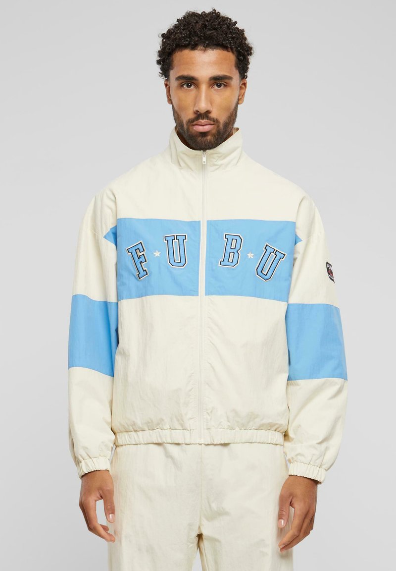 Light cream jacket featuring a blue horizontal band with navy lettering "FUBU." Full zip, elastic cuffs, and slightly textured fabric.