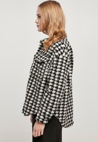 Sort-hvid houndstooth mønstret jakke med krave, struktureret stof og afslappet pasform; sidevisning der viser form og designdetaljer.