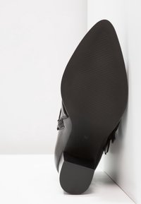 Černá kožená bota s nízkým podpatkem, s texturovanou gumovou podrážkou. Design zahrnuje jemný akcent s detailem přezky. Velikost 37.