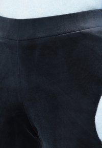 Tumši zili samta bikses ar gludu tekstūru un pieguļošu dizainu. Redzami šuves un smalka spīduma efekts uzlabo materiāla izskatu.