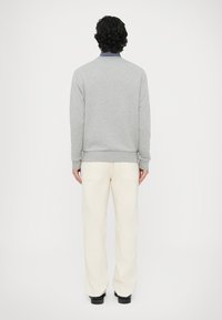 Szara bluza z prążkowanymi mankietami i ściągaczem, noszona z kremowymi spodniami. Strój charakteryzuje się prostym wzorem i luźnym krojem.