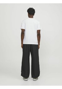 Camiseta de algodón blanca con mangas cortas, combinada con pantalones negros holgados. Los pantalones tienen un diseño de pierna ancha y bolsillos laterales.