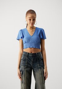 Blå kort topp med V-hals, korte pufferm, og teksturert stoff; parret med mørke denim cargo bukser med sidelommer.