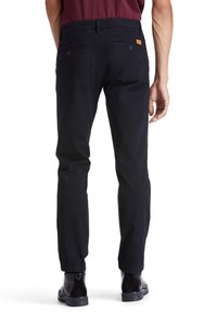 Navy blue trousers with a straight cut and a textured fabric. Features back pockets and a small leather patch logo near the waistband.