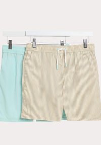 Två par shorts hängde på klämmor: ett par ensfärgat mintgrönt, det andra beige med vertikala ränder. Båda har elastiska midjeband och snörning.